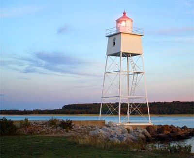 The Grand Marais Harbor of Refuge Outer Lighthouse stands along Lake Superior at sunset.
